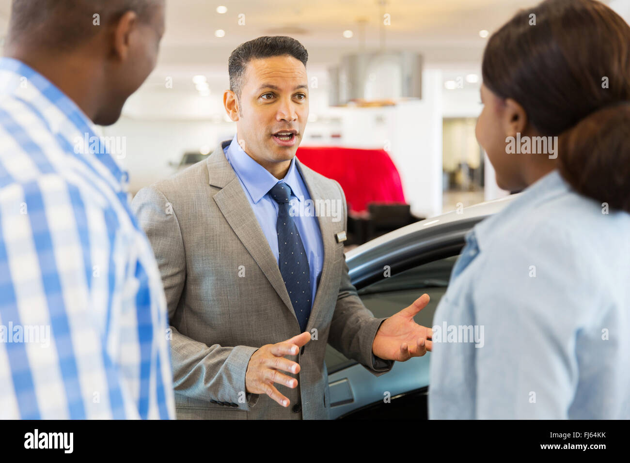 middle aged car salesman talking to African couple inside showroom Stock Photo