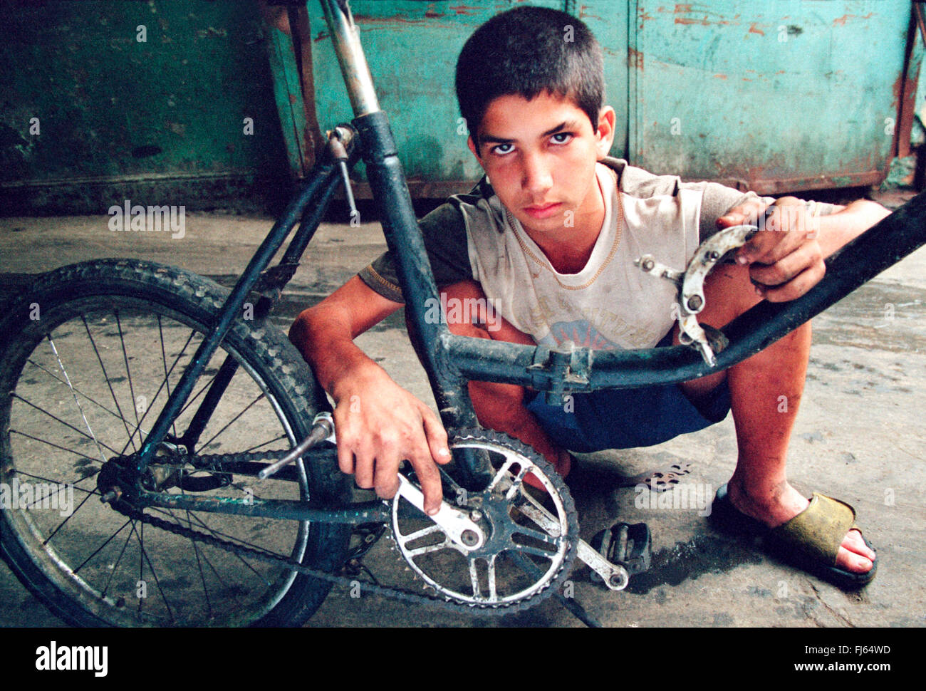 Cuban boy Fernando Castillo repairing his bicycle on a garage entrance., Cuba Stock Photo