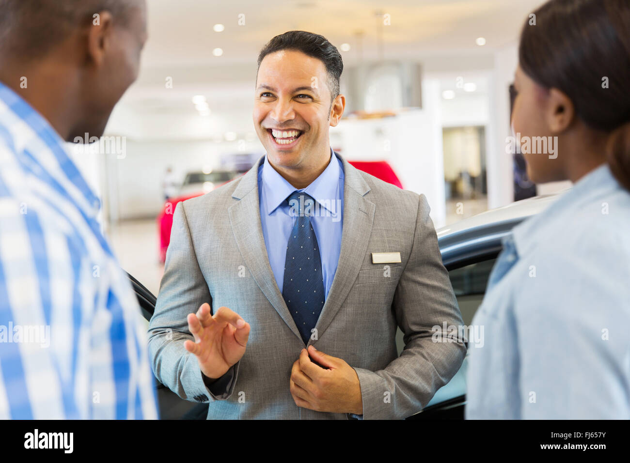 handsome vehicle dealer talking to customers in showroom Stock Photo
