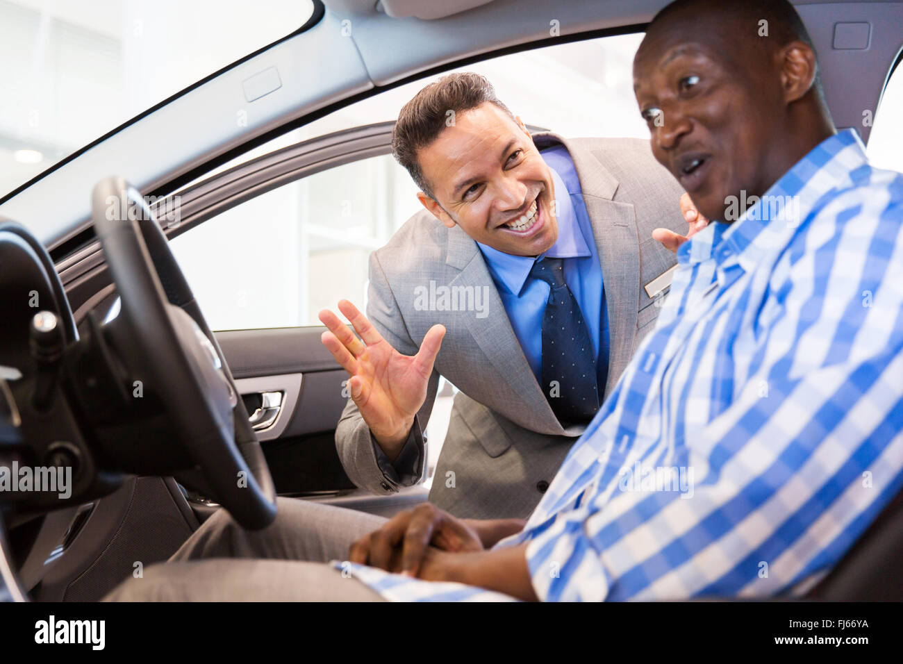middle aged salesman showing new car interior to customer sitting inside the car Stock Photo