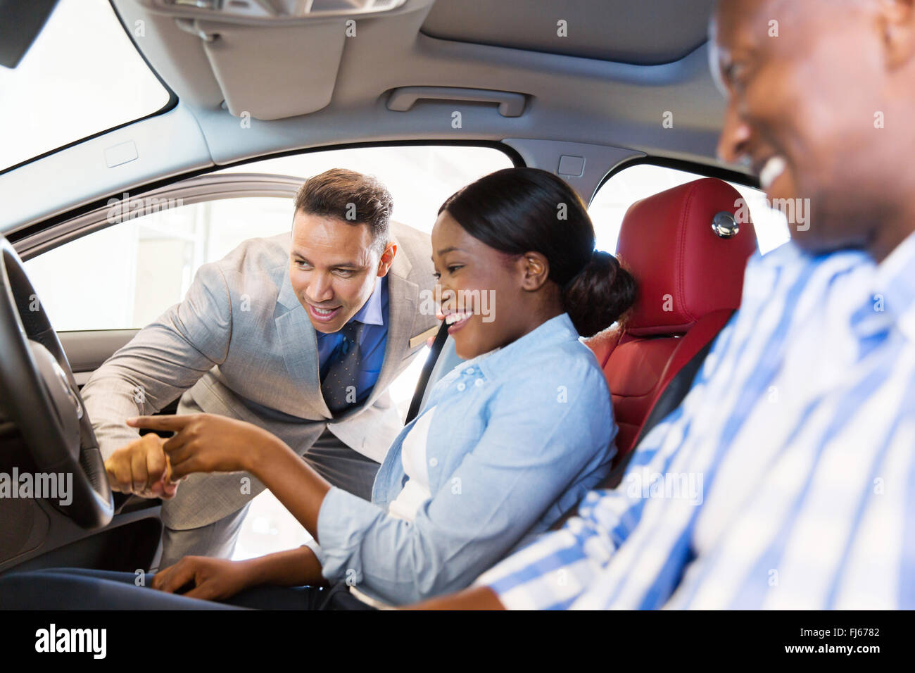 salesman showing new car to African couple in showroom Stock Photo