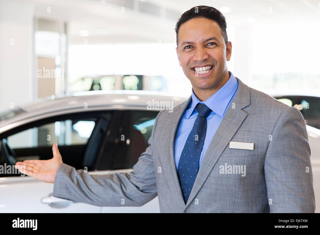friendly car salesman welcoming gesture at car dealership Stock Photo