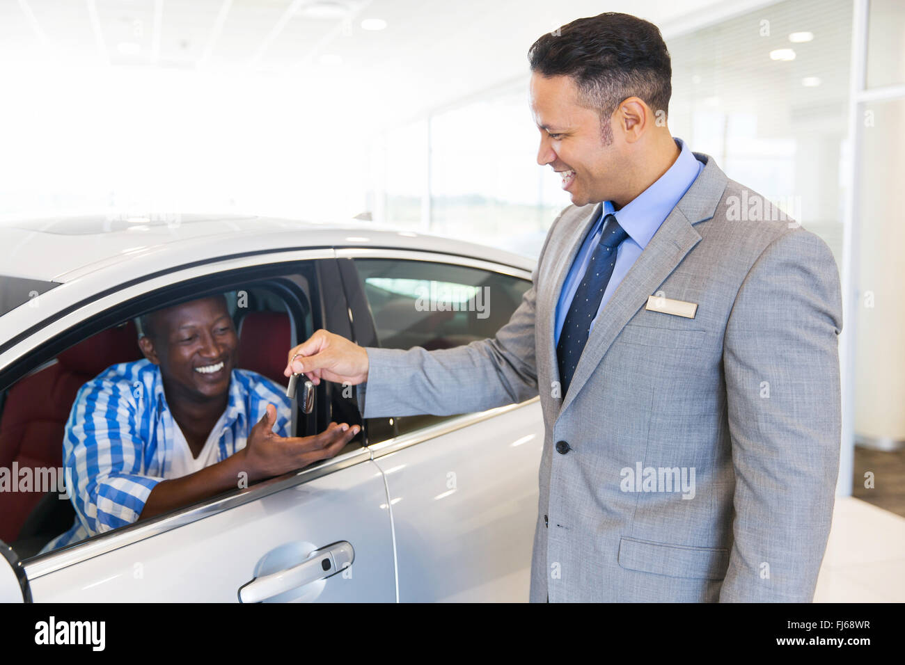 car salesman handing over new car key to customer sitting inside vehicle at showroom Stock Photo