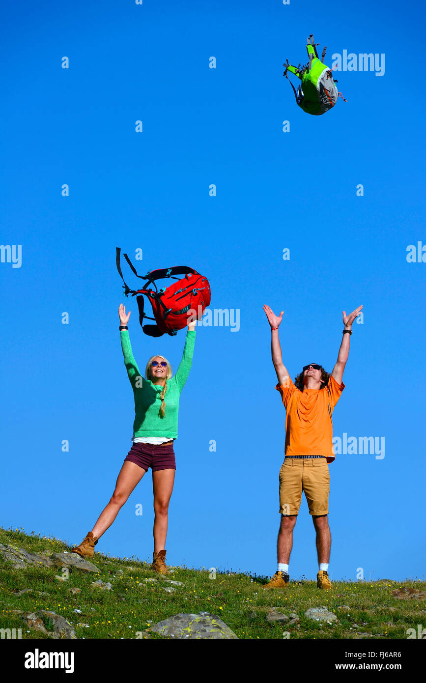 two young people throwing up for joy their rucksacks , France, Savoie Stock Photo