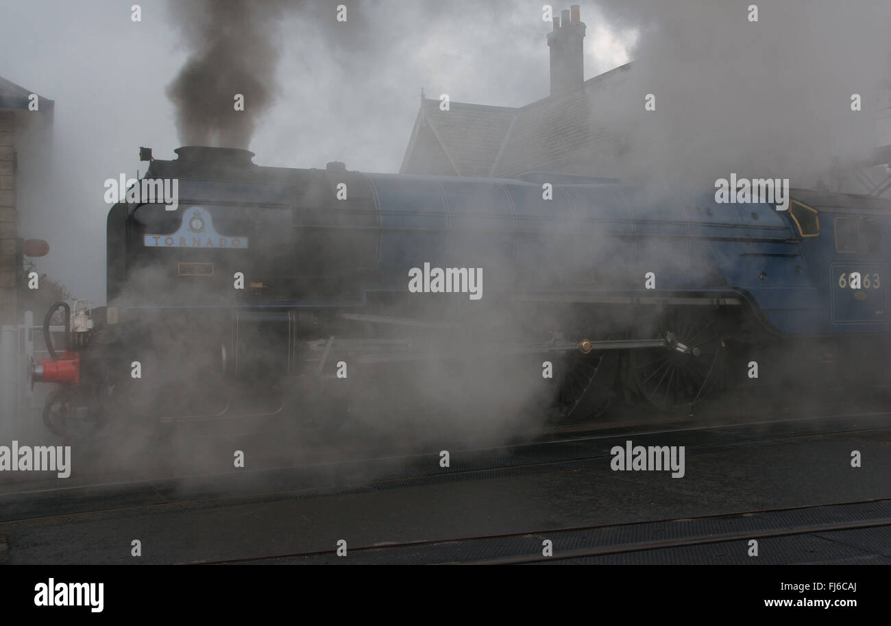 Atmospheric photo of Tornado steam locomotive in BR blue shrouded in steam leaving Grosmont Station,  North York Moors Railway Stock Photo