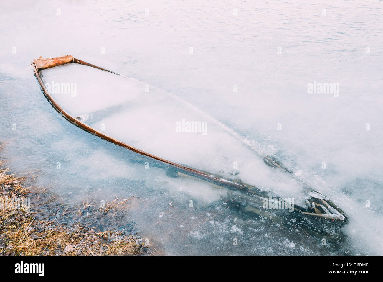 Frozen into ice of river, lake, pond old wooden boat. Abandoned rowing fishing boat in winter river. Forsaken boat Stock Photo
