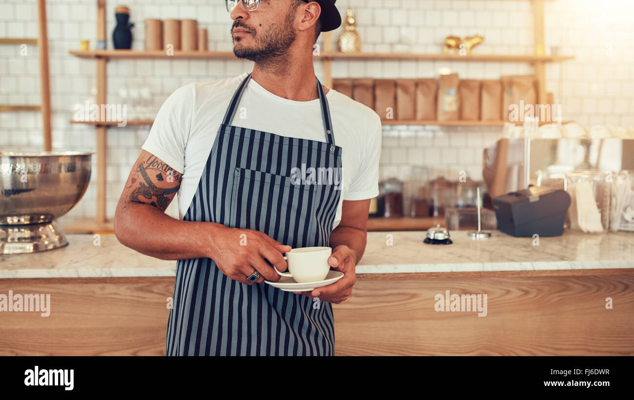 Cropped portrait of young man standing at cafe counter and looking away. Male at working in coffee shop. Stock Photo