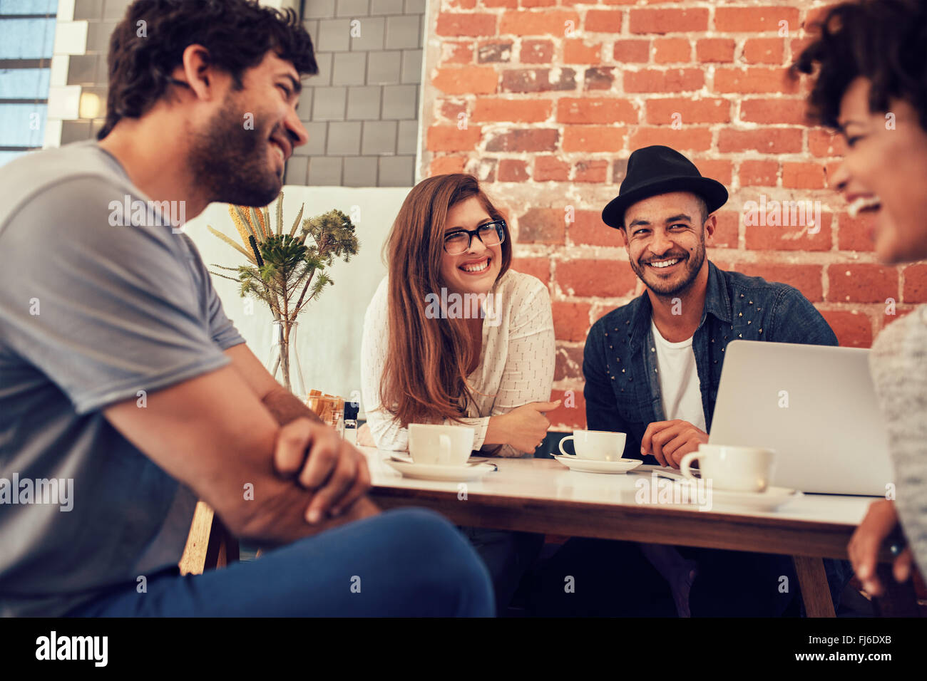 Group of young friends hanging out at a coffee shop. Young men and women meeting in a cafe having fun. Stock Photo