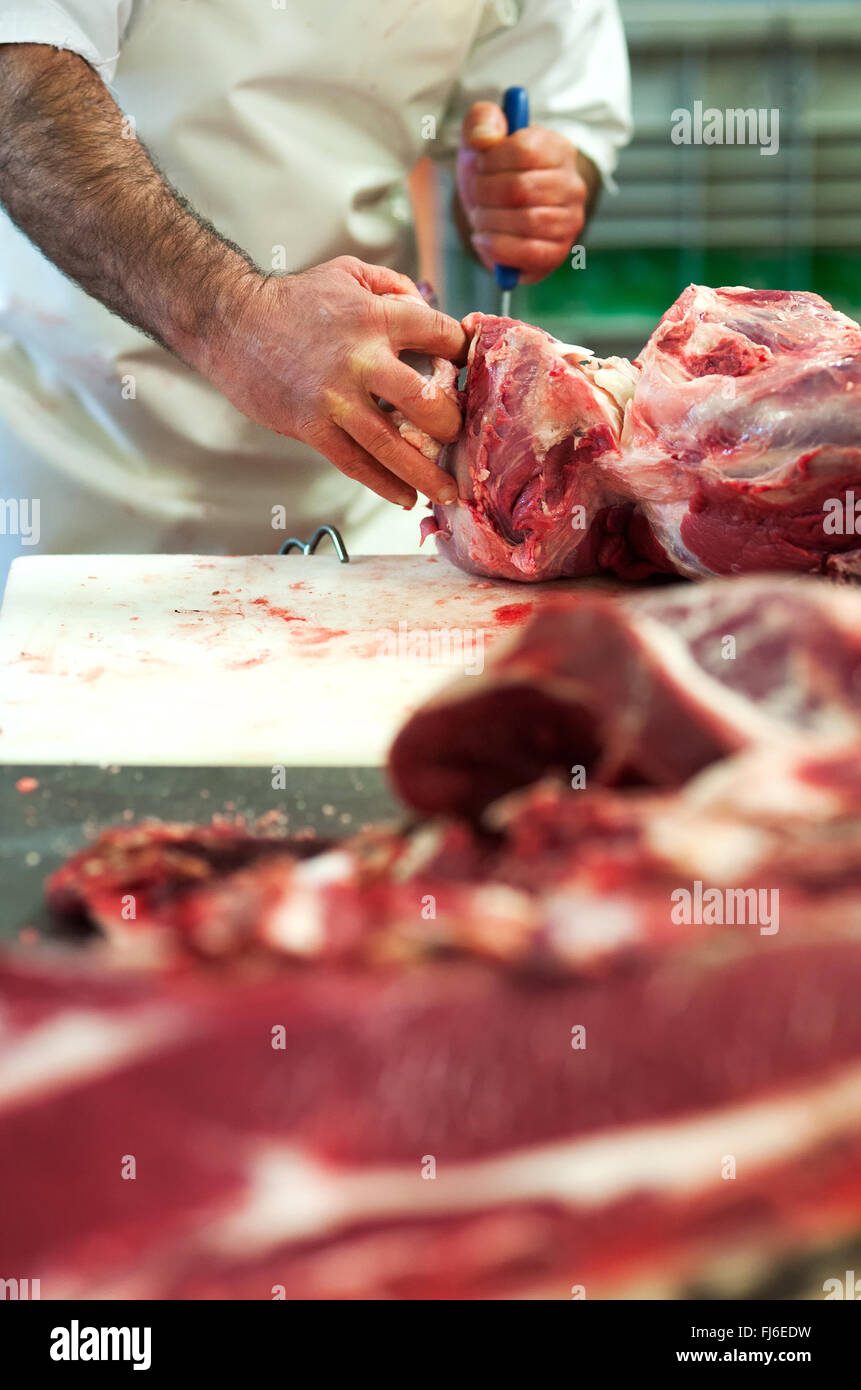 Butcher cutting up raw meat in a butchery using a knife Stock Photo