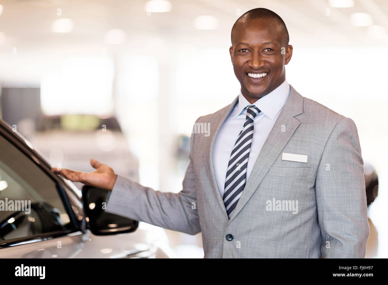 friendly African car dealer presenting new vehicle in showroom Stock Photo