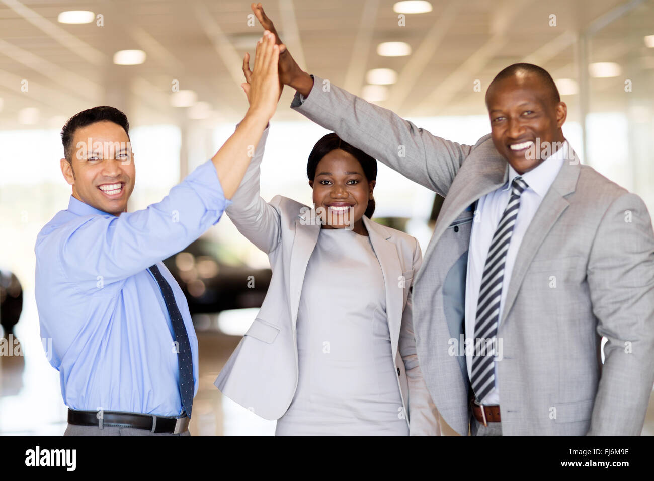 successful car dealership staff giving high five in showroom Stock Photo