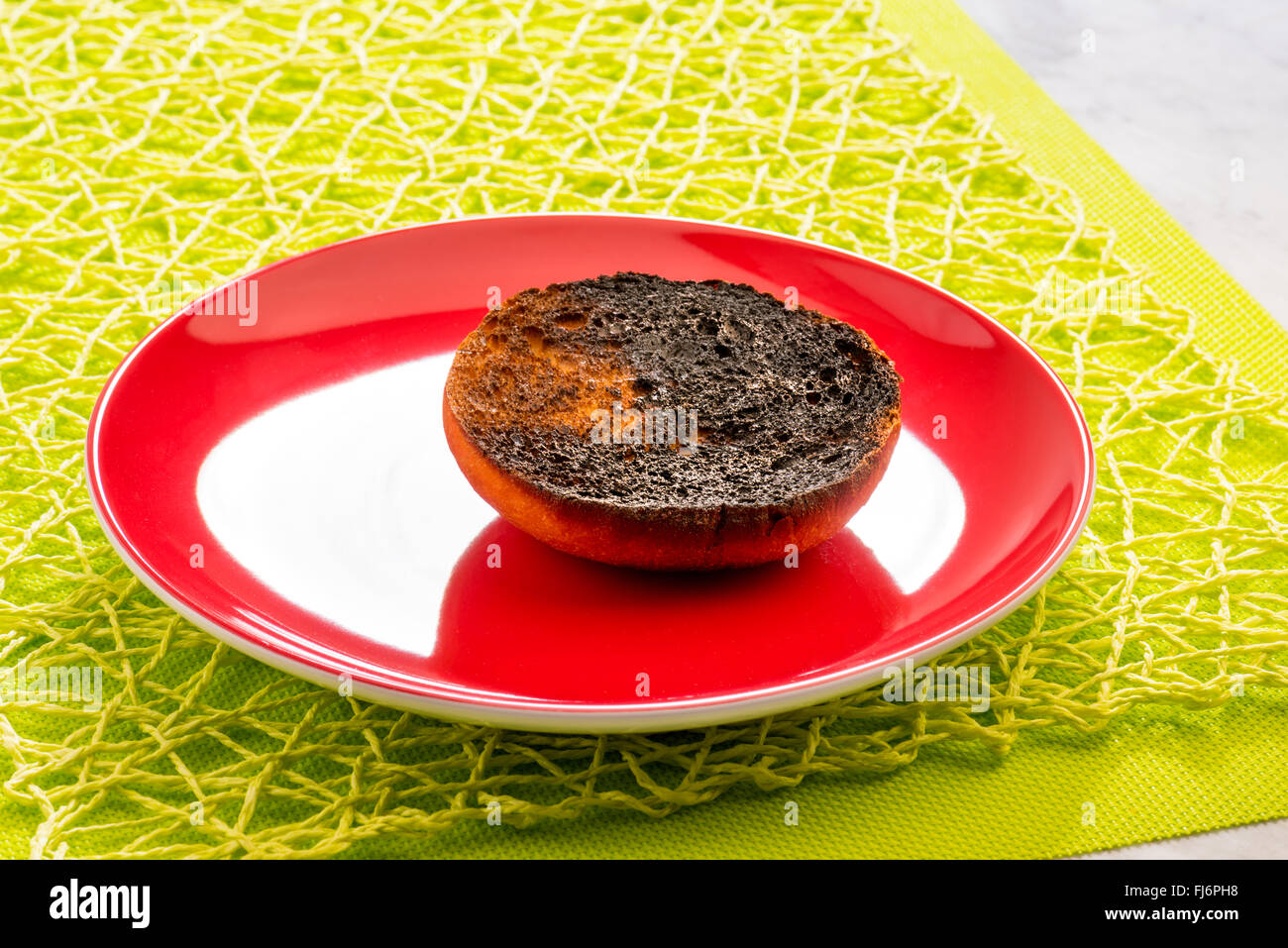burnt toast, slice, since the toast is burned black, ruined, inedible, coal, on red plate, green background, spring, breakfast, Stock Photo