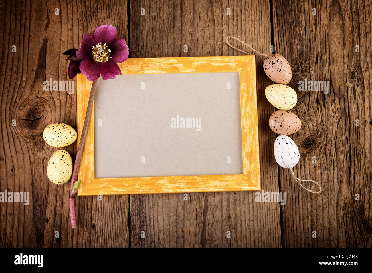 Easter greeting card with yellow picture frame on old wooden board. Top view with copy space. Stock Photo