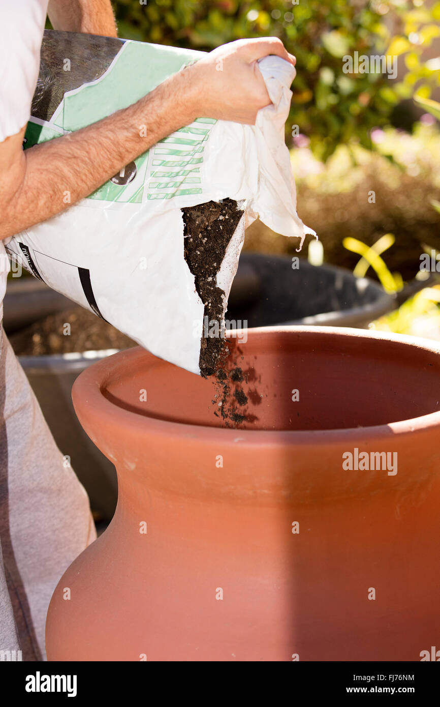 A man preparing a clay pot for a garden by creating a hole and base in ground, then filling and planting with garden soil Stock Photo