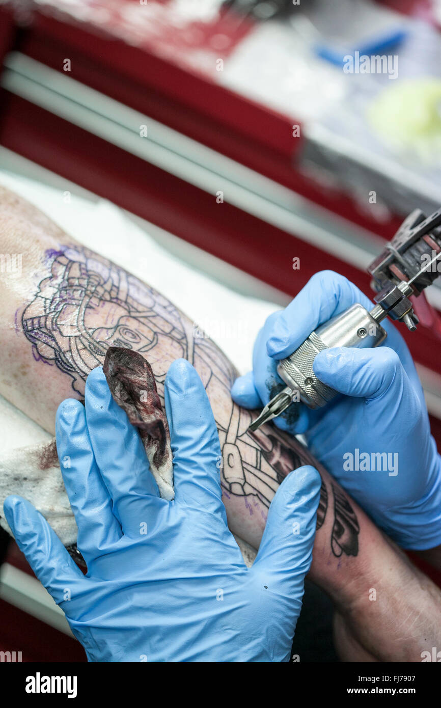 Tattoo artist wearing blue latex gloves tattoos a bio-mechanical images on clients arm Stock Photo