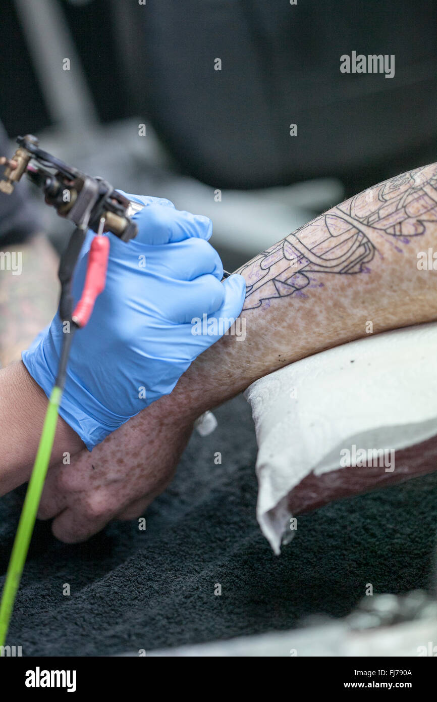 Tattoo artist wearing blue latex gloves tattoos a biomechanical images