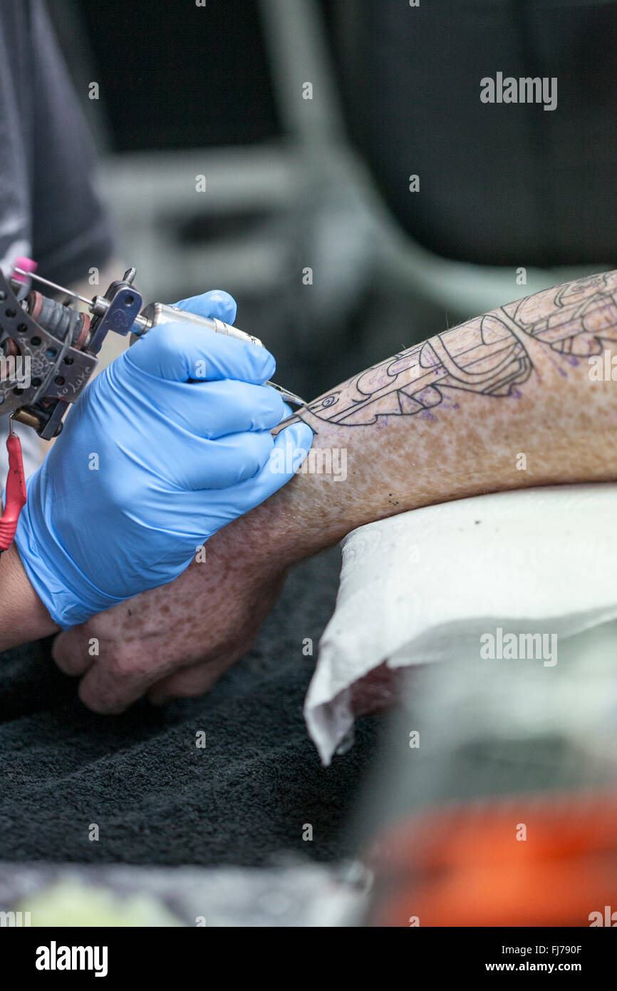 Tattoo artist wearing blue latex gloves tattoos a biomechanical images