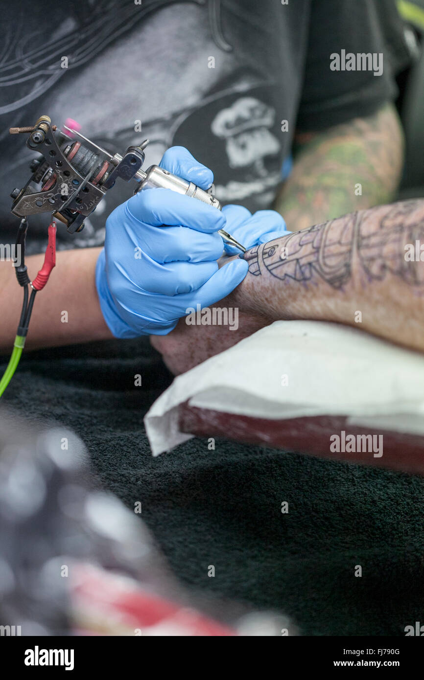 Tattoo artist wearing blue latex gloves tattoos a biomechanical images