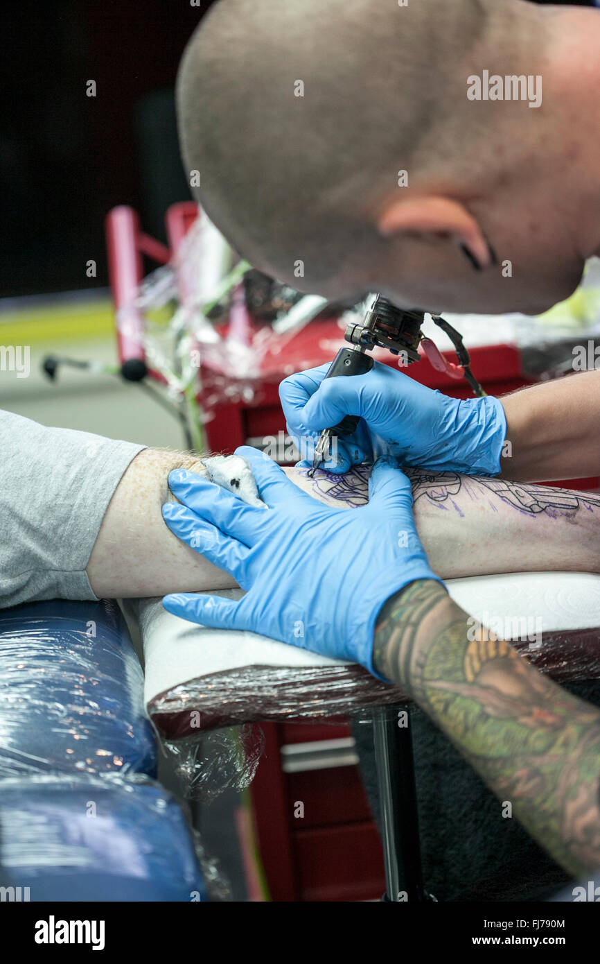 Tattoo artist wearing blue latex gloves tattoos a biomechanical images