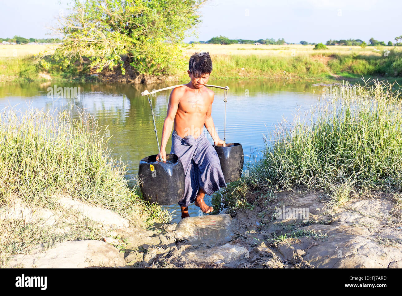 Water carrier with two buckets getting water in the countryside from Myanmar Stock Photo