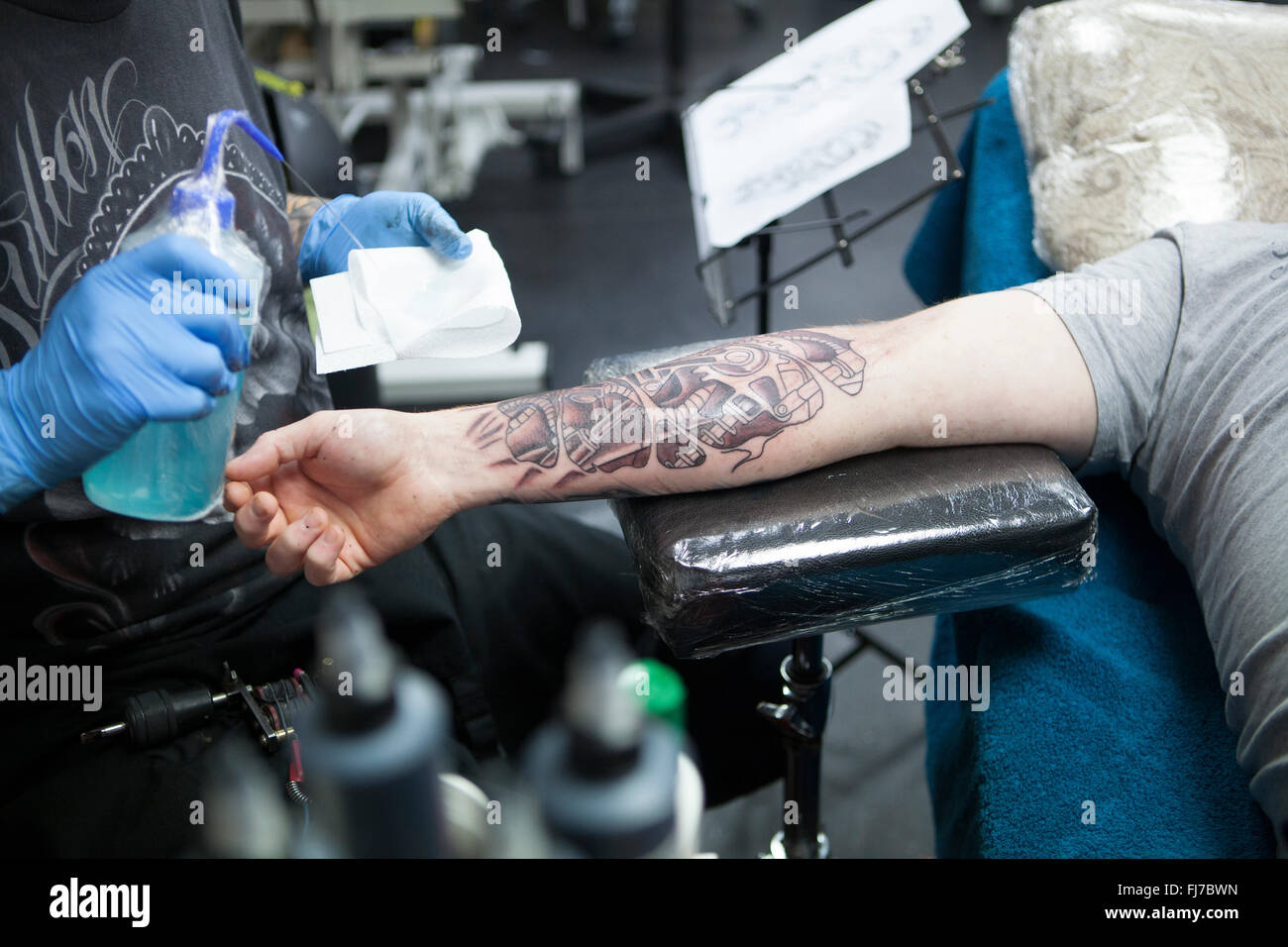 Tattoo artist wearing blue latex gloves tattoos a biomechanical images