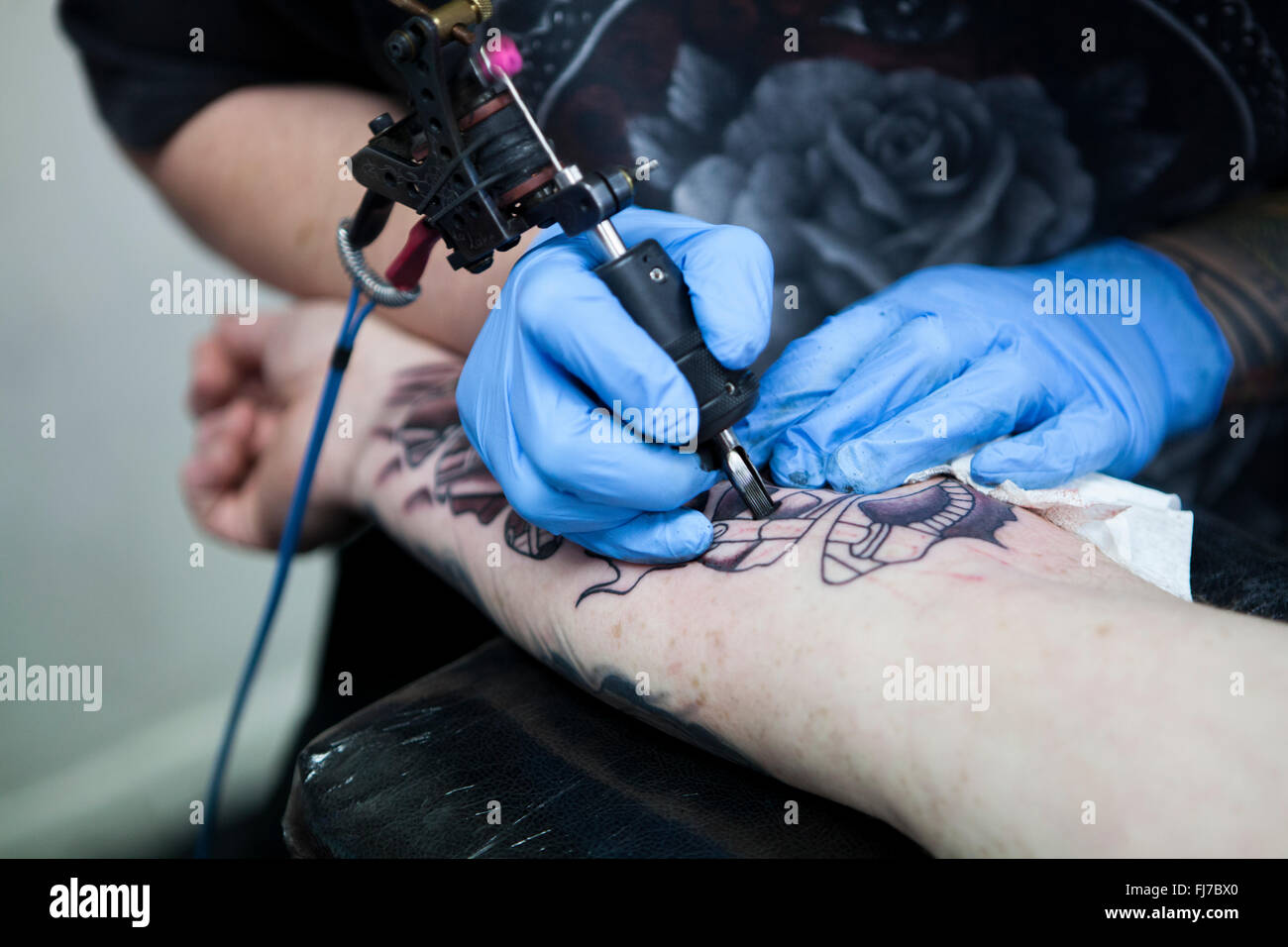 Tattoo artist wearing blue latex gloves tattoos a bio-mechanical images on  clients arm Stock Photo - Alamy
