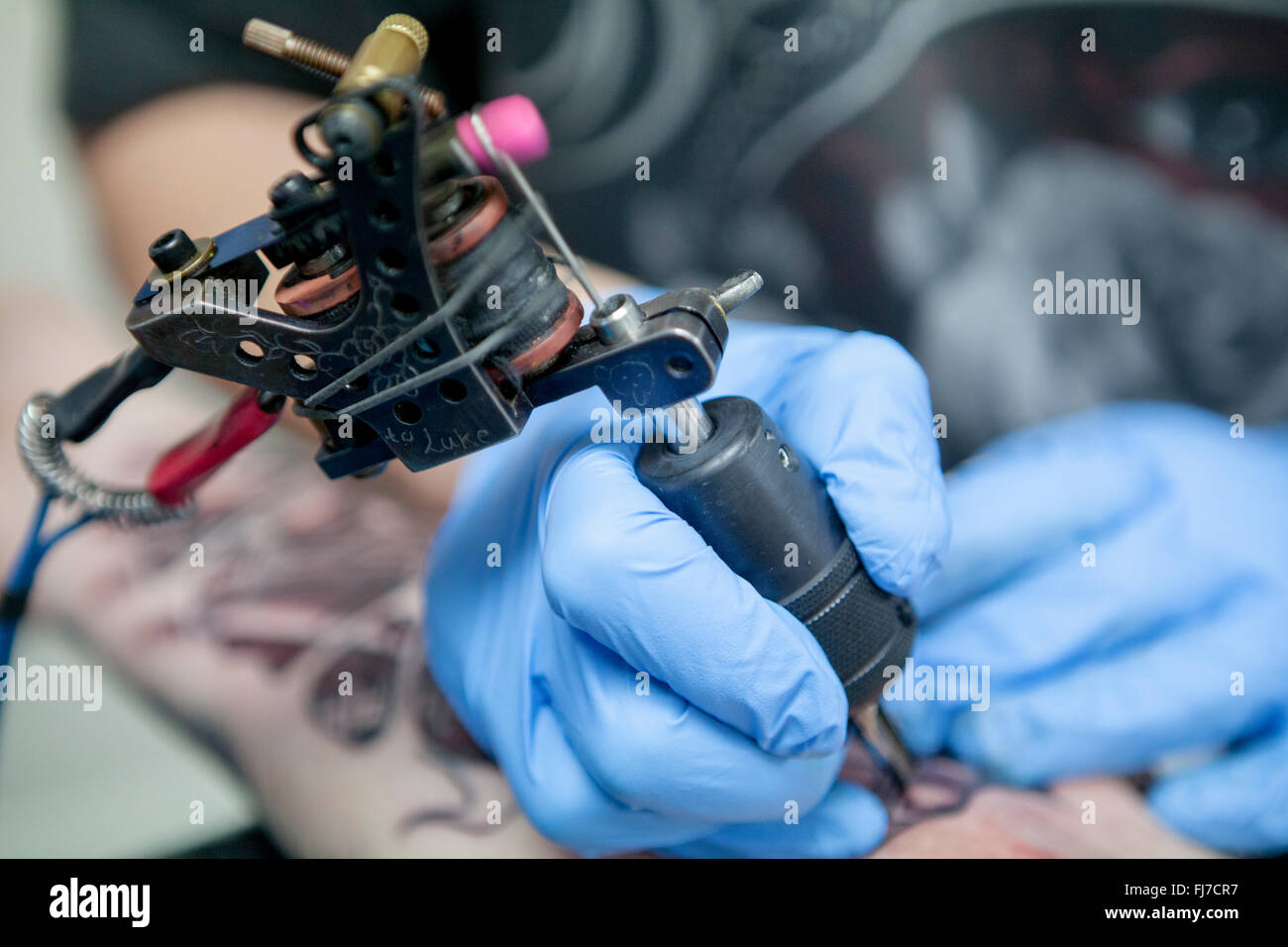 Tattoo artist wearing blue latex gloves tattoos a bio-mechanical images on clients arm Stock Photo