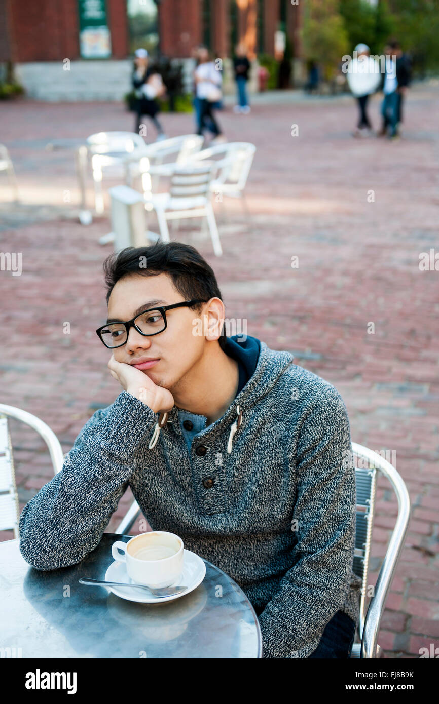 Young asian man in outdoor cafe with cup of coffee looking away being bored and unhappy Stock Photo