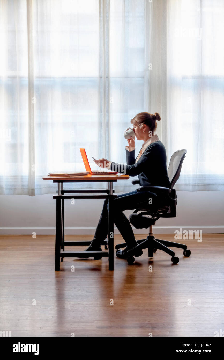A woman sitting at a computer with window behind her Stock Photo