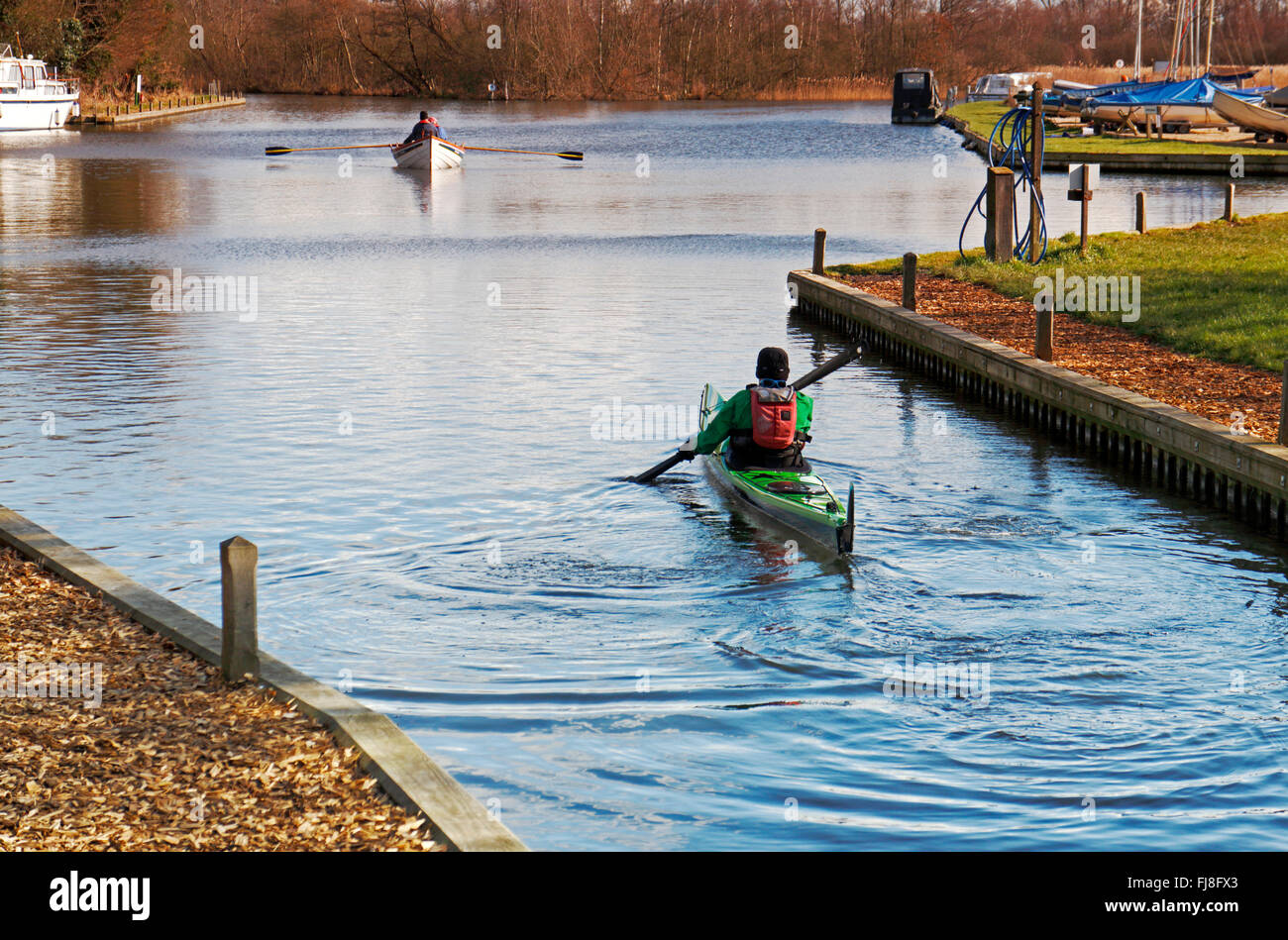 A canoeist and rowers on the Norfolk Broads in winter at Barton Turf Staithe, Norfolk, England, United Kingdom. Stock Photo