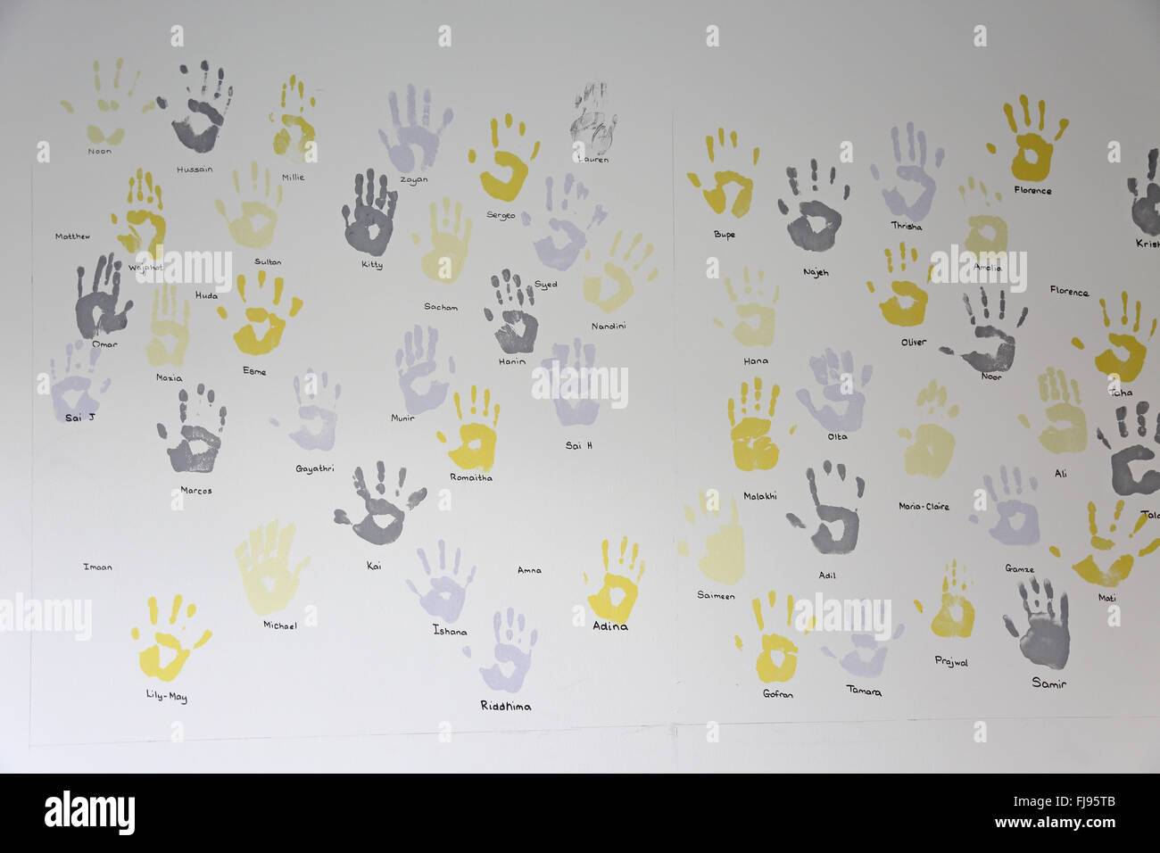 children's palm prints in grey and yellow paint on the wall of a new school. Names are written below each print. Stock Photo
