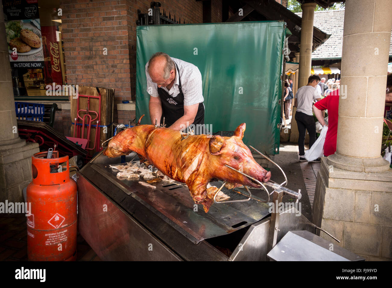 A man cutting meat from a roasted hog on a spit, Stroud Farmer's Market, Gloucestershire Stock Photo