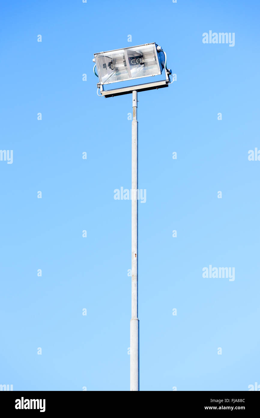 A tall floodlight on a lamp post against clear blue sky. Copy space on both sides. Stock Photo