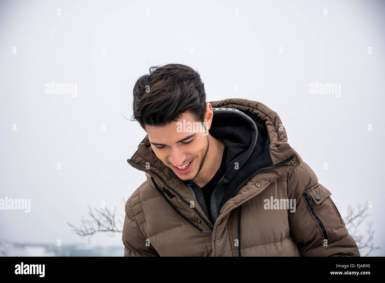 Handsome man in outerwear sitting while looking at camera. Snowy landscape on background Stock Photo