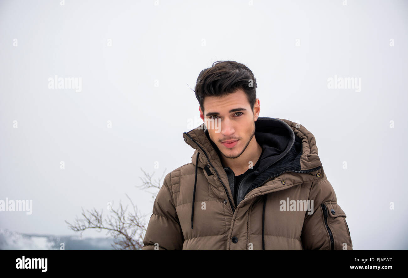 Handsome man in outerwear sitting while looking at camera. Snowy landscape on background Stock Photo