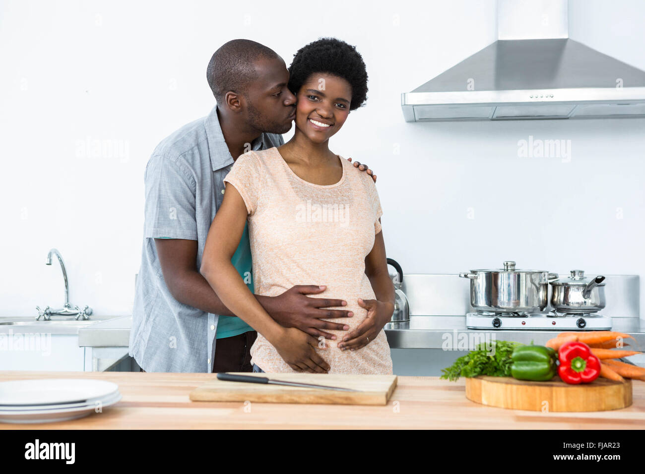 Pregnant couple embracing in kitchen Stock Photo