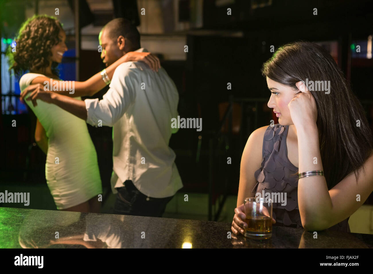 Unhappy woman looking at a couple dancing behind her Stock Photo