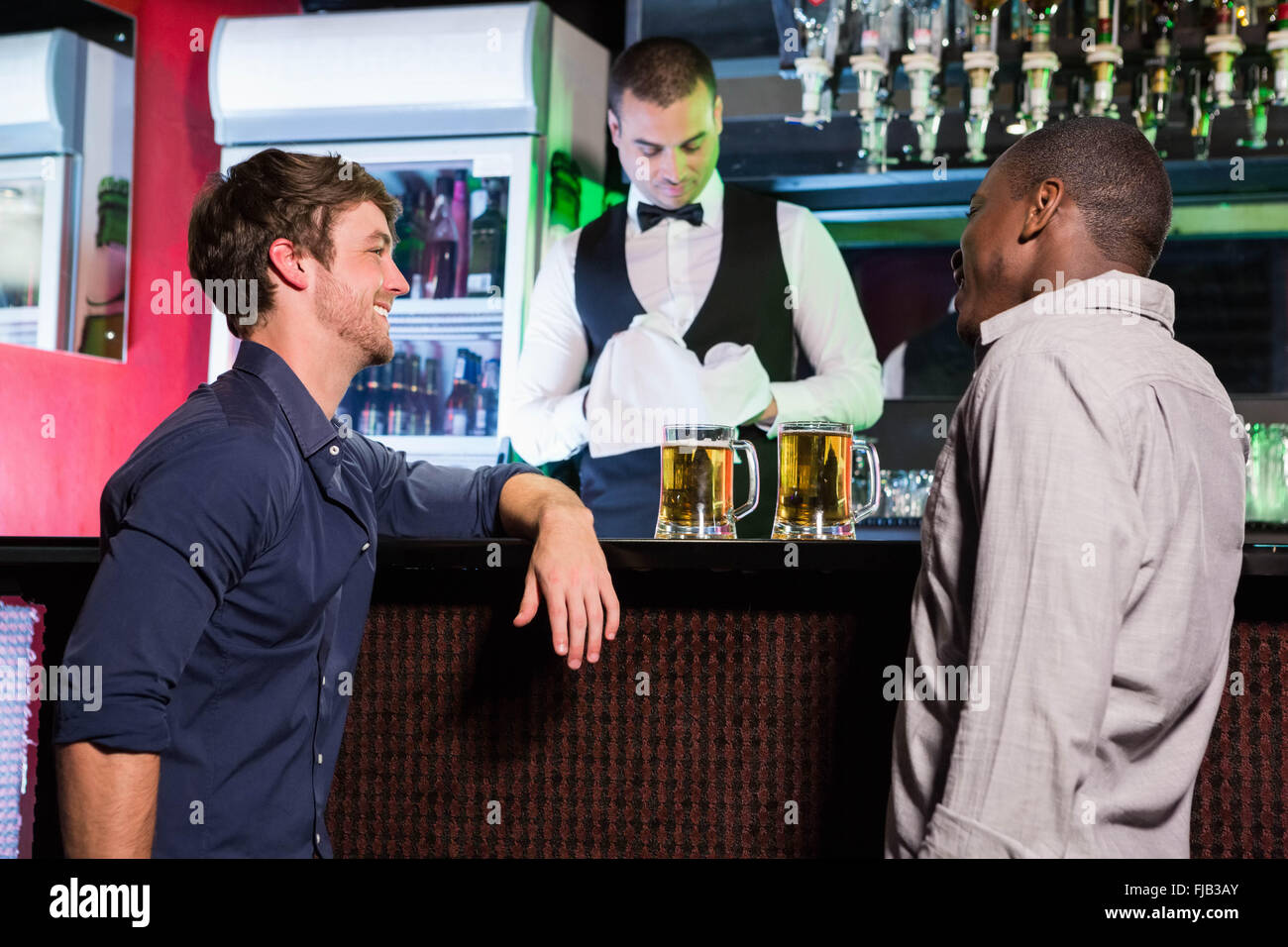 Two men smiling and talking to each other while having beer at bar counter Stock Photo