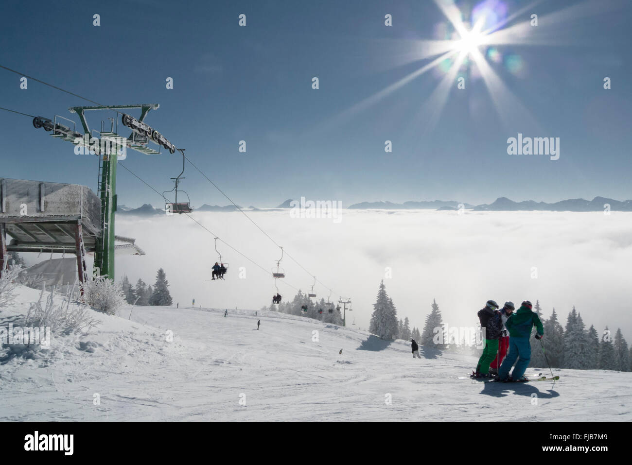 Skiers standing next to a chair lift in front of the alpine panorama at Brauneck ski resort in bright sunlight,Bavaria,Germany Stock Photo