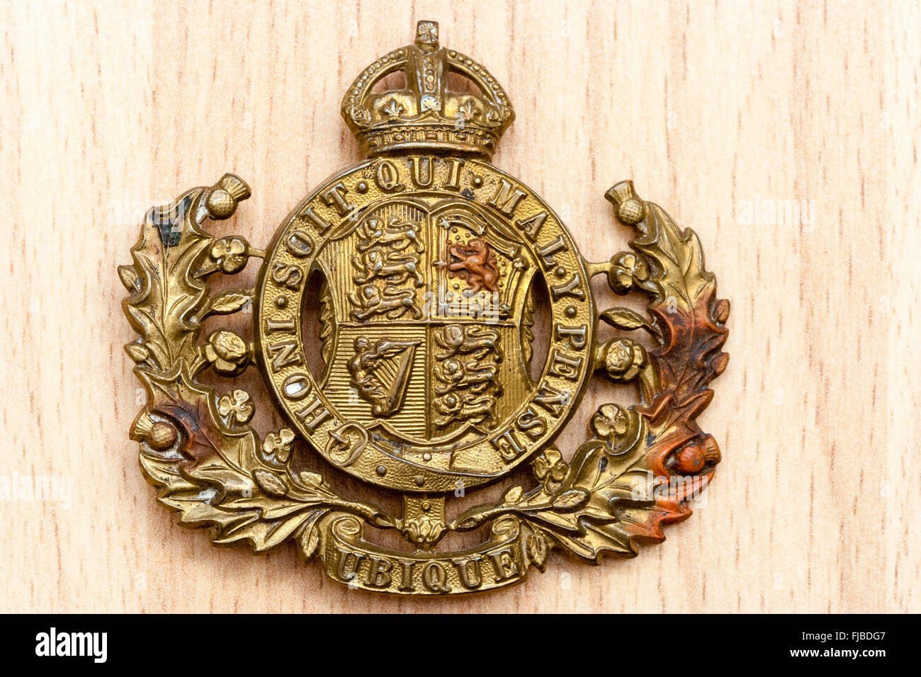 Royal Artillery Ubique cap Badge from the first world war against wooden grain background. Badge features motto 'honi soit qui mal y pense'. Stock Photo