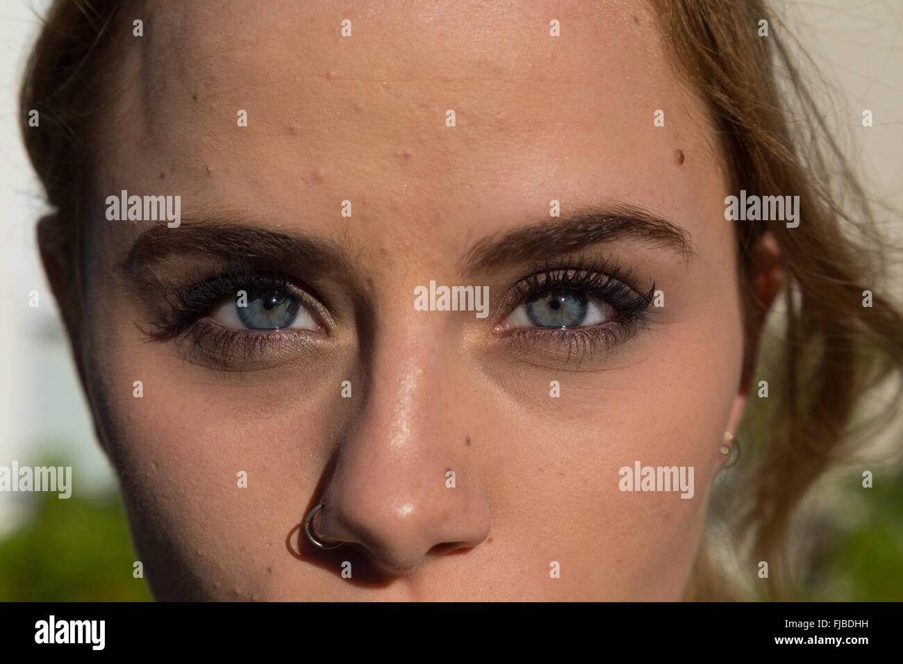 Close up of a beautiful woman's face with stunning blue eyes and a pierced nose. Stock Photo