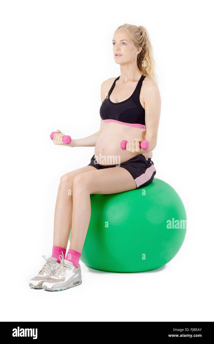 Pregnant woman on yoga balance ball performing bicep curl exercise with weights. Stock Photo