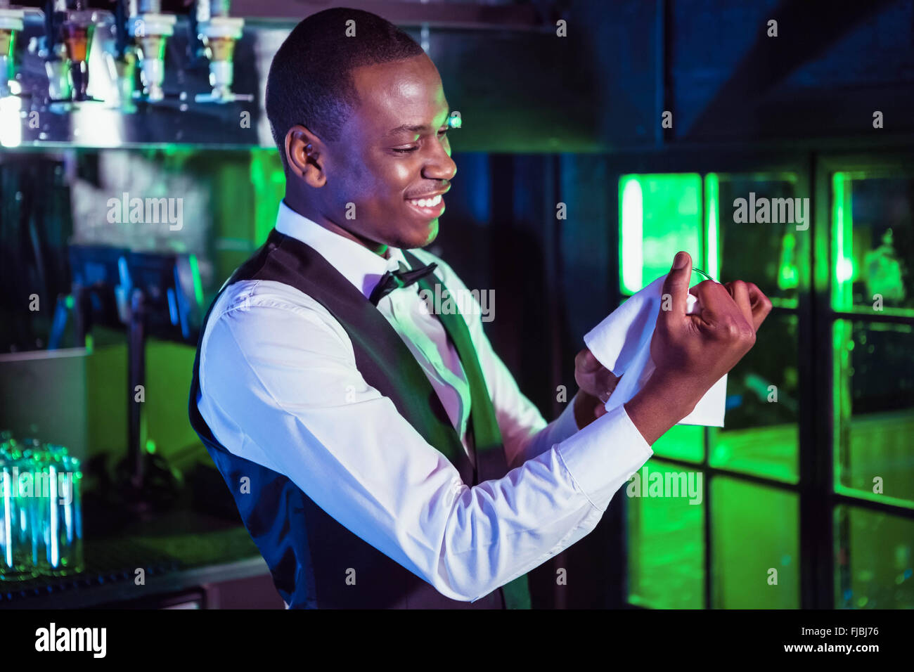 Smiling male bartender wiping a glass and looking away. Barista in