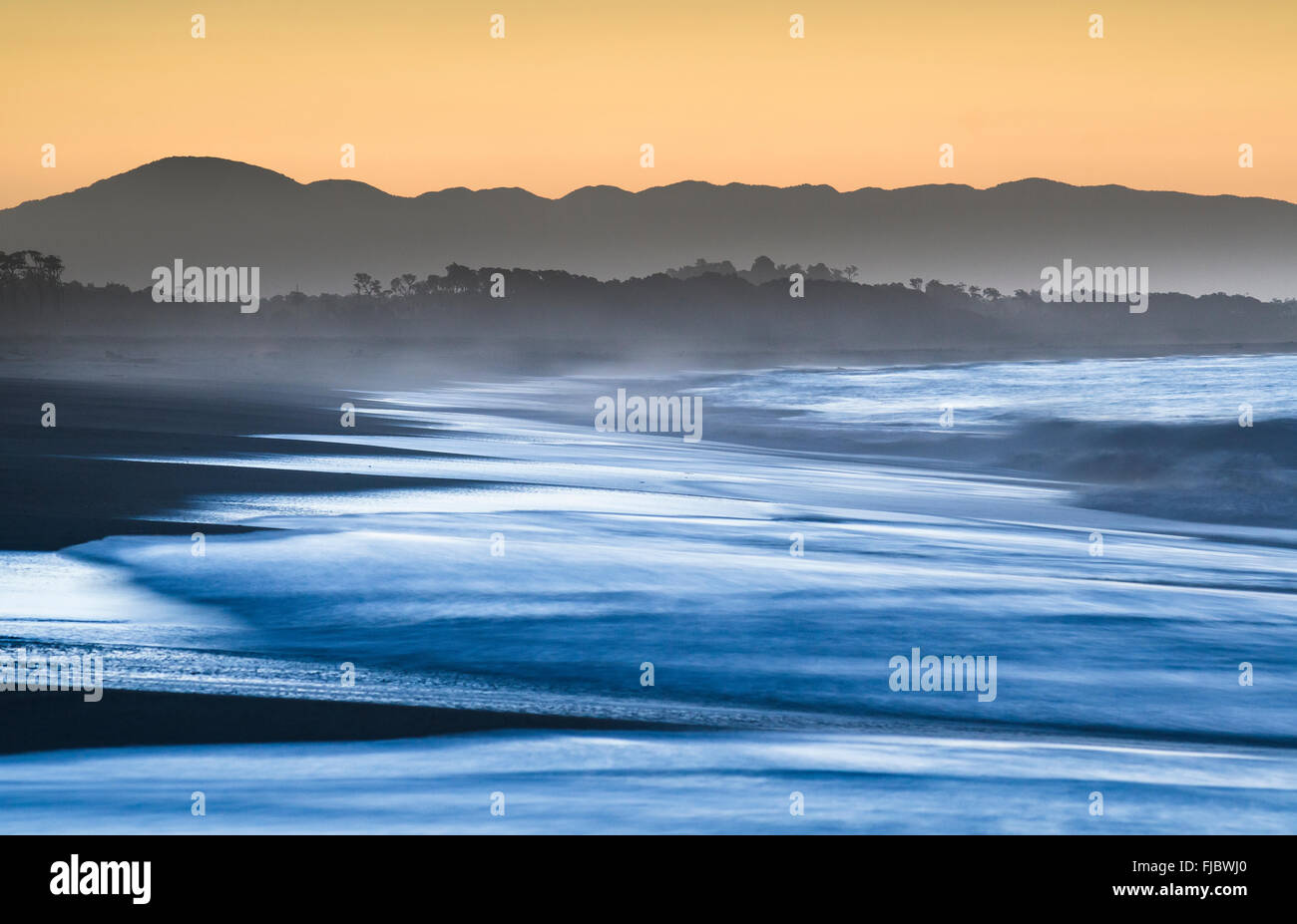 Surf with haze on a wide beach in the evening light, sunset in Haast, West Coast, South Island, New Zealand Stock Photo