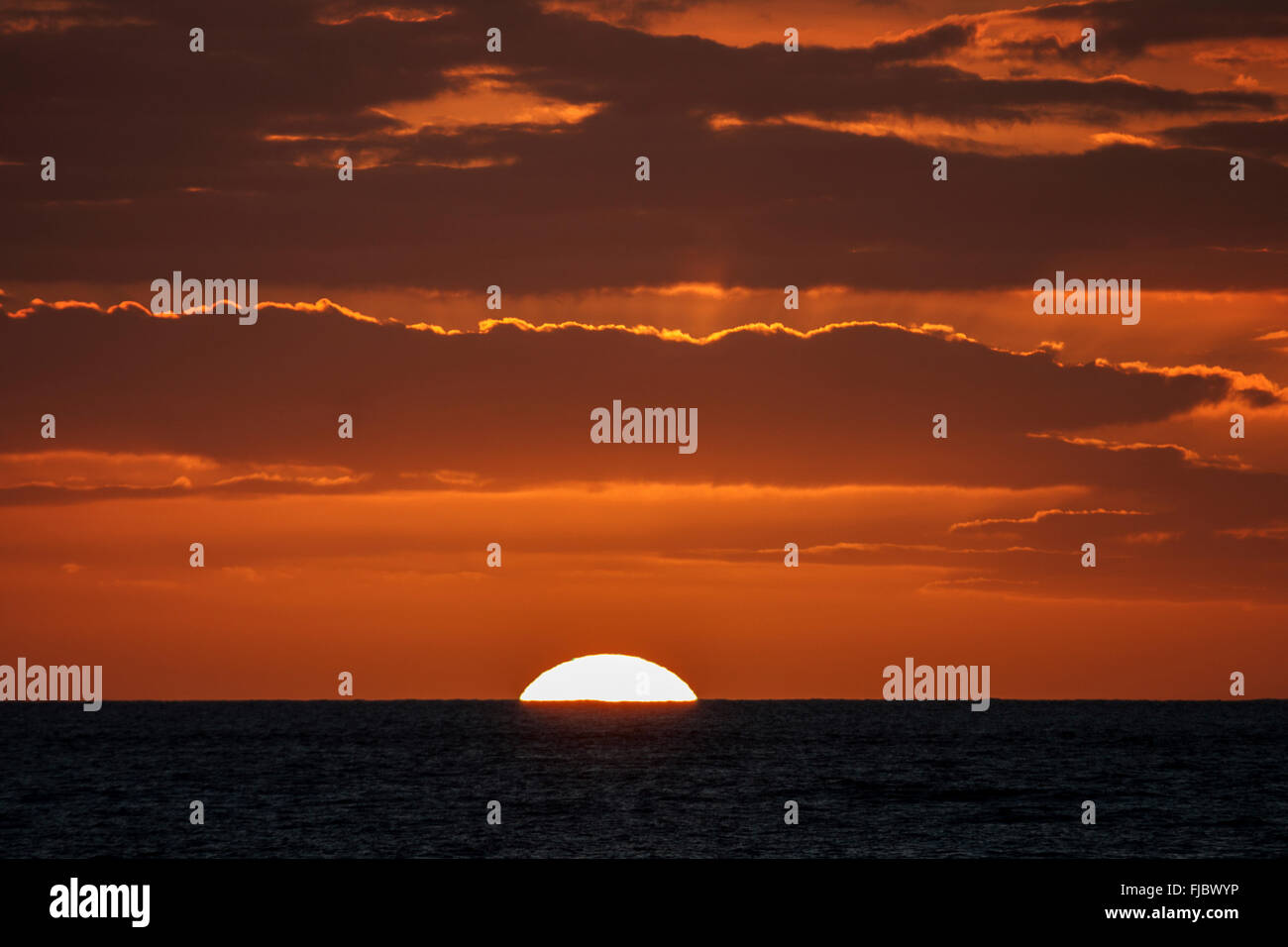 Sunset with clouds, sun sinking into the sea, near Saint-Gilles-Les-Bains, Réunion Stock Photo