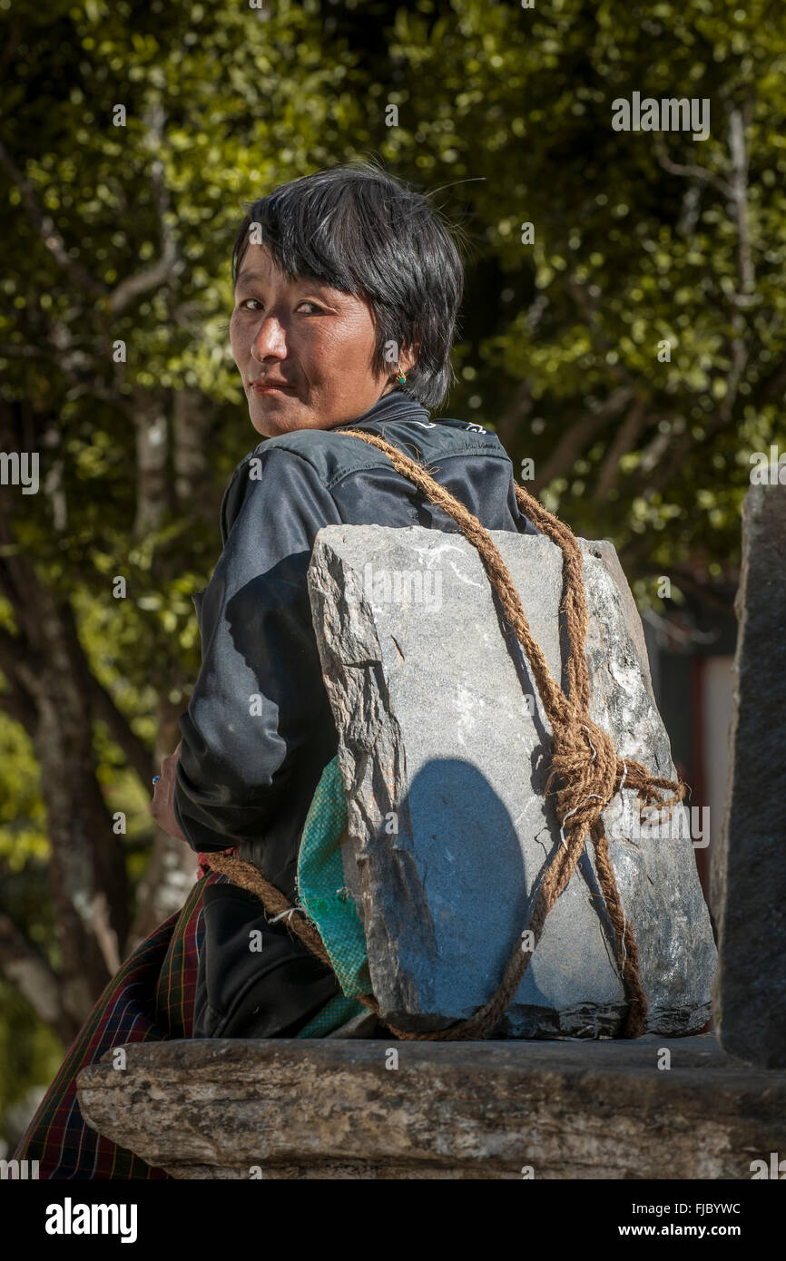 A woman taking a rest, with building materials, a stone slab on her back, Himalayas, Kingdom of Bhutan Stock Photo
