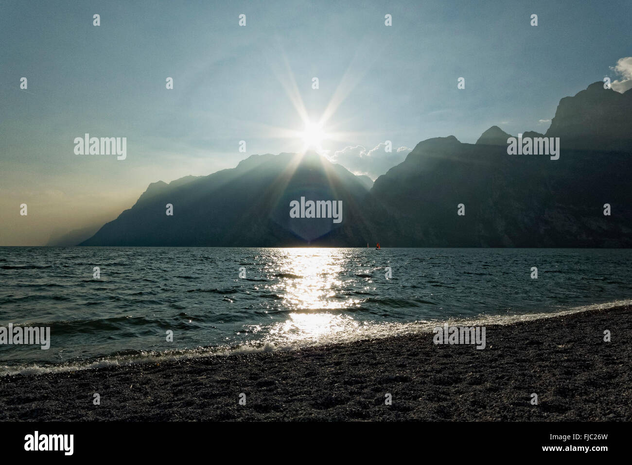 Strand, Sonne über den Bergen, Torbole, Gardasee, Trentino, Italien | Beach, sun over the mountains, Torbole, Lake Garda, Trenti Stock Photo