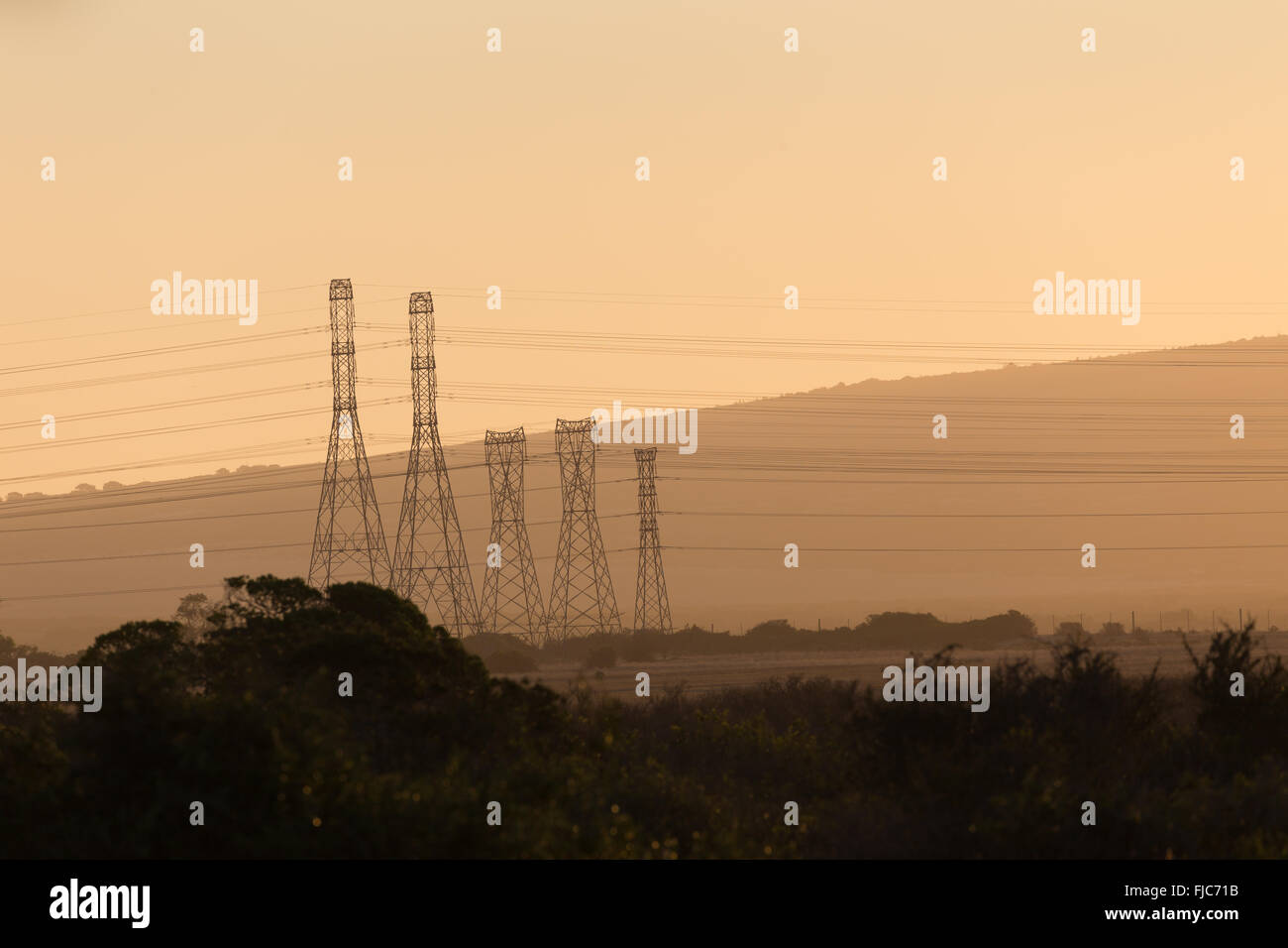 Power pylons during a misty orange sunset Stock Photo