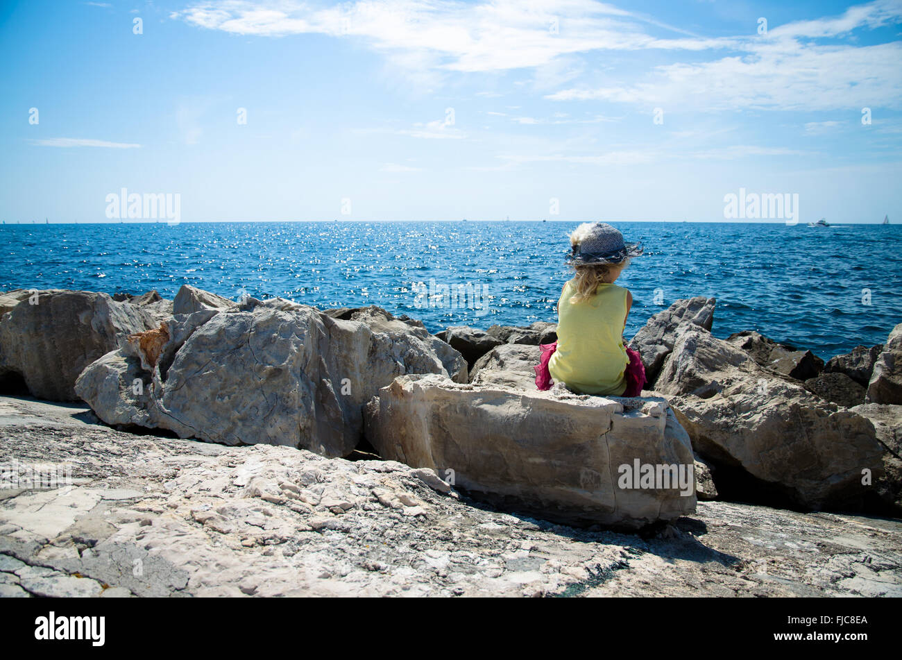 little girl sitting in the rock observing blue sea Stock Photo - Alamy