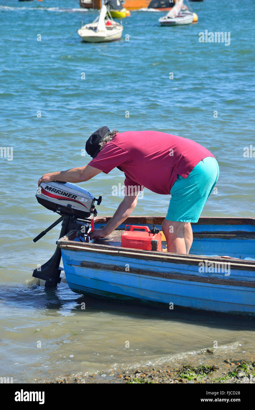 Man adjusting outboard on tender on Itchenor hard/slipway, Chichester, West Sussex, UK, Great Britain Stock Photo